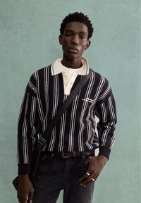 Maglione a righe blu navy e crema con scollo a collo, abbinato a jeans scuri. Cintura e borsa a tracolla completano il look.