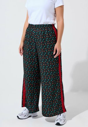 Mustat leveät housut, joissa on punaisia ja vihreitä kukkakuvioita, joustava vyötärö ja punaiset sivupinnat. Yhdistetty valkoisiin tennareihin.