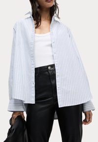 Camisa de botones de gran tamaño a rayas azul y blanca con cuello extendido, mangas largas y dobladillo ligeramente Curvado, combinada con pantalones de cuero negros.