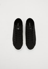 Une paire de baskets noires basse de Calvin Klein avec des semelles blanches et des lacets noirs, vues de dessus sur un fond blanc.