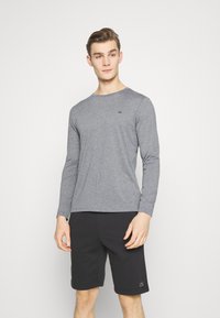 Gray long-sleeve shirt featuring a round neckline and a small CK logo, paired with black shorts, displayed against a white background.