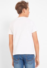 T-shirt bianco in cotone con maniche corte, design semplice e collo rotondo. Indossato con jeans in denim blu con tasche posteriori cucite.
