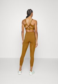 Sostén deportivo marrón con tirantes cruzados en la parte posterior, combinado con leggings de tiro alto a juego, todo en una tela suave y elástica. Zapatos ligeros.