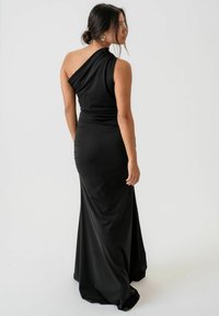 Fekete, egyvállas estélyi ruha sima anyagból. Feszülő sziluettel rendelkezik, hátul ráncolt díszítéssel és egy lágyan folyó szoknyával.