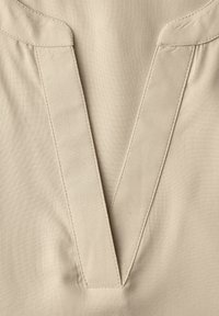 Gros plan sur un tissu beige avec un détail de col cousu en forme de V sur un vêtement, mettant en valeur la texture et les lignes de couture.