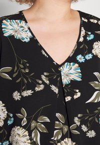 Czarna bluzka z dekoltem w serek, zdobiona białymi, niebieskimi i zielonymi kwiatami; gładka tekstura i luźny krój.