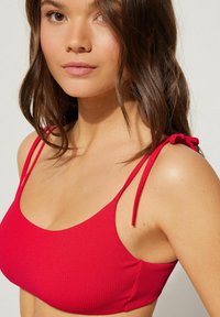 Červený pruhovaný crop top s tenkými nastavitelnými ramínky, zaobleným výstřihem a měkkou texturou, s přiléhavým střihem.