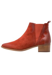 Botas de ante rojas hasta el tobillo con puntera redondeada, paneles laterales elásticos y un tacón de bloque de madera. Presentan recortes decorativos en el cuero.