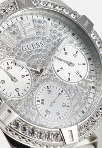 Orologio da polso argento con una lunetta decorata di cristalli, tre quadranti secondari e un quadrante testurizzato con motivi circolari e numeri audaci.