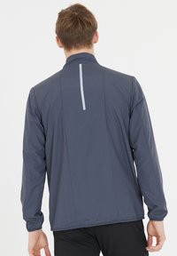 Laivastonsininen urheilu takki, jossa on pystykaulus, pitkät hihat, heijastava pystysuora raita ja sileä, kevyt kangas, jossa on hieno tekstuuri.