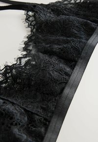 Svart spetsbralette med blommönster, med justerbara remmar och en satingjord. Mjuk textur med intrikata detaljer och fransiga kanter.