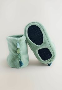 Pantofole verdi in peluche con una texture morbida, dotate di frange decorative sul retro e una suola in gomma scura.