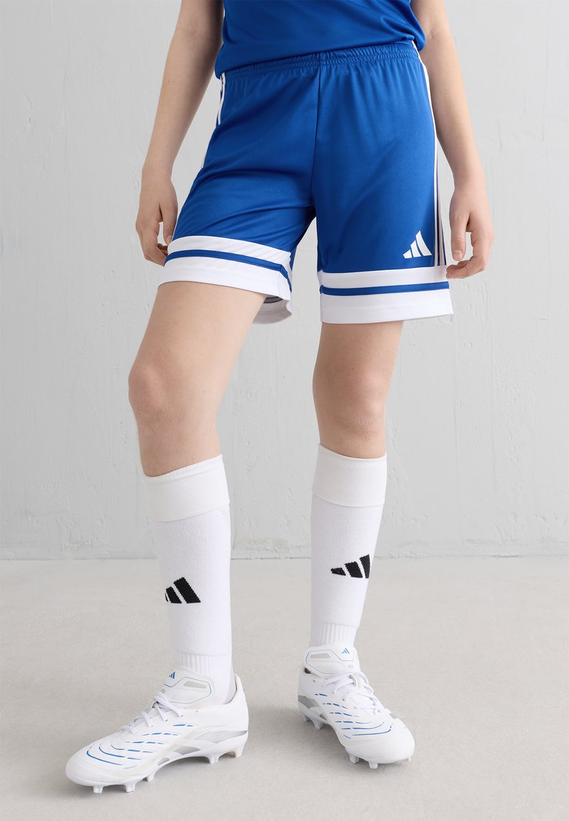 Blå idrottsshorts med vita ränder i fållen, tillsammans med vita strumpor med svarta detaljer. Skorna är vita fotbollsskor med blå detaljer.