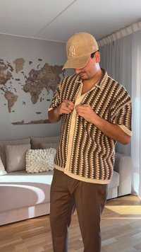 Camicia a maniche corte con bottoni, con motivo geometrico marrone, crema e beige; abbinata a pantaloni marroni; tessuto texturizzato; vestibilità casual.