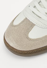 Sneaker con puntale in suede beige, tomaia in pelle bianca e lacci bianchi. Suola in gomma con un motivo testurizzato per una presa migliore.