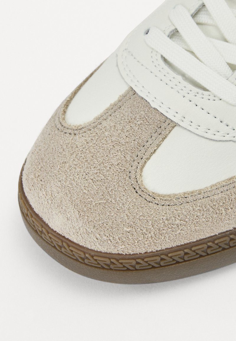 Sneaker mit einer beigen Wildlederzehenkappe, einem weißen Lederoberteil und weißen Schnürsenkeln. Gummisohle mit einem strukturierten Muster für besseren Halt.