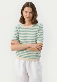 Sweter z krótkim rękawem w paski w miętowym zielonym i kremowym kolorze, z prążkowanym dekoltem i wykończeniem. Gładka faktura, noszony z jasnymi spodniami.