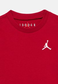 Κόκκινη βαμβακερή μπλούζα με στρογγυλή λαιμόκοψη, με λευκό κεντητό λογότυπο Jumpman στη αριστερή πλευρά του στήθους. Ομαλή υφή.