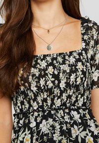 Svart blommig klänning med smockad bodice och fyrkantig halsringning. Korta puffärmar, har vita och gula blommor med gröna blad.