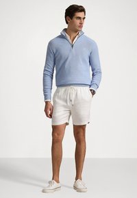 Ανοιχτό μπλε πουλόβερ με φερμουάρ στον γιακά, συνδυασμένο με λευκά σορτς. Τα παπούτσια είναι λευκά αθλητικά. Απλός σχεδιασμός και άνετη εφαρμογή.