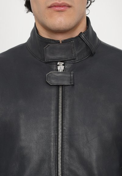 Veste en cuir noir avec un col haut, fermeture éclair à l'avant et double boucle de fermeture. Texture lisse avec un minimum de détails et une coupe ajustée.