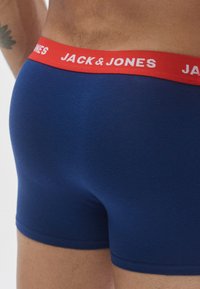 Cuecas boxer azuis com uma cintura elástica vermelha com a inscrição "JACK & JONES" em letras brancas. Tecido liso e design ajustado.