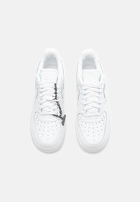 Hvite lærersneakers med perforert tåboks, flate hvite snøringer og et s�ølvkjede som aksent på snøringene. Minimalistisk design.