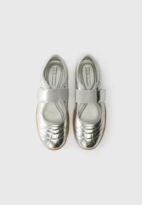 Silver metallic Mary Jane shoes with a rounded toe, pleated design, and an adjustable gray strap across the instep. Natural rubber sole.