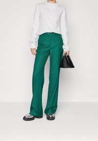 Zelené široké kalhoty v kombinaci s texturovaným bílým pleteným svetrem, doplněné o robustní černé boty a malou černou kabelku.