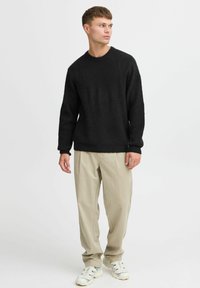Black textured sweater with a crew neck, paired with light beige trousers. The outfit features a relaxed fit and casual sneakers.