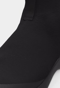 Κοντινό πλάνο ενός μαύρου παπουτσιού σε στυλ κάλτσας με ριγωτό ύφασμα και ταινία για τραβήγμα στην πίσω φτέρνα.