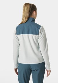 Chaqueta de forro polar en gris claro con una sección superior azul. Presenta un cuello alto, mangas largas y una textura suave.