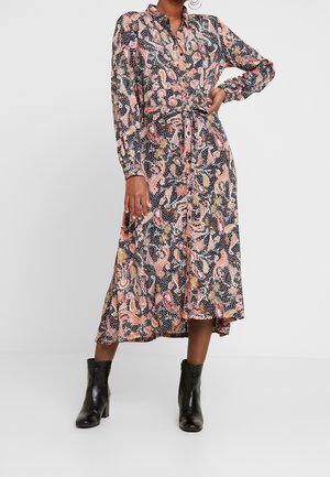 Woman wearing a long-sleeve, buttoned black dress with pink paisley and white dots pattern, paired with black heeled ankle boots.