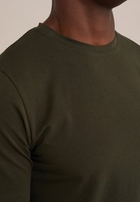 Olivově zelené tričko s krátkým rukávem vyrobené z jemné bavlny, s klasickým kulatým výstřihem a hladkou, rovnoměrnou strukturou.