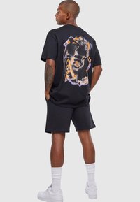 Black cotton T-shirt with a large graphic print in orange and purple on the back, paired with black shorts and white sneakers.