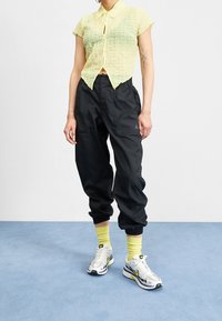 Yellow textured short-sleeve shirt, black loose jogger pants, and white sneakers with gray and neon accents. Accessories include bright socks.