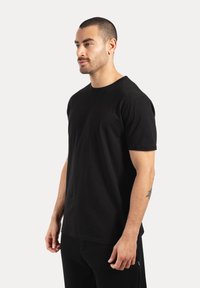 Camiseta de algodón negra con mangas cortas, cuello redondo y un corte relajado, mostrada en una persona sobre un fondo neutro.