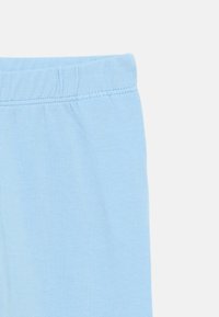 Hele sinised puuvillased retuusid, millel on elastne vöökoht ja sile tekstuur, kaunistatud lihtsa õmblusega äärtes.