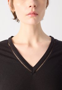 Top nero a scollo a V realizzato in tessuto morbido; presenta una finitura in rete dettagliata lungo il colletto, una texture liscia e un design aderente.