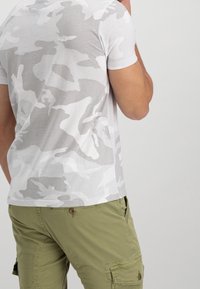 Camiseta de rayas de camuflaje gris claro hecha de algodón suave, de mangas cortas, combinada con pantalones cortos cargo verde oliva con bolsillos laterales.