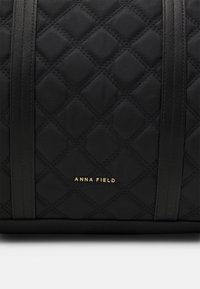 Borsa a spalla in nylon nero trapuntato con manici neri e logo dorato "ANNA FIELD." Caratterizzata da un motivo a rombi e una texture liscia.