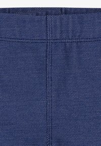 Sötétkék denim szövet, szoros twill szövésű, látható varrással és sima textúrával, finom elhalványulással a varratok mentén.