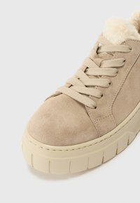 Beige suede sneaker with a textured surface, cream faux fur collar, and thick, light-colored rubber sole. Features beige laces.