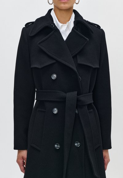 Cappotto nero doppiopetto realizzato in tessuto texturizzato, con ampi rever, tasche laterali, vita con cintura e dettagli in metallo.