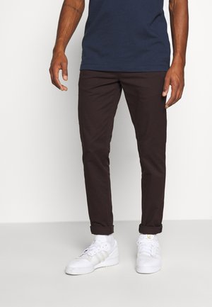 Marineblauw T-shirt met korte mouwen gecombineerd met donkerbruine chinos, opgerolde pijpen en witte sneakers met drie strepen en veters.