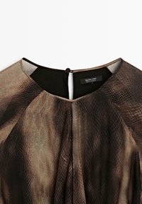 Robe avec un motif peau de serpent marron et noir, tissu doux, encolure arrondie et fermeture par boucle à l'arrière. Étiquette visible.