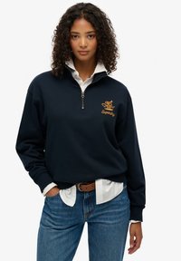 Marine blauwe zip-up sweatshirt met ribgebreide manchetten, voorzien van een geborduurd logo in goud. Draag het over een wit shirt en combineer het met blauwe jeans.