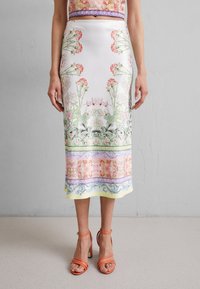Jupe midi en soie avec motifs floraux roses et verts, bordée de motifs décoratifs dans des couleurs pastel. À assortir avec des talons à brides orange.