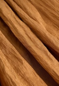 Barna árnyalatú, gyűrött szövet, amely változatos redőkkel és enyhe fényességgel rendelkező texturált felületet mutat, alkalmas rétegezésre vagy felakasztásra.