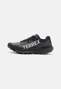 Black athletic shoe with gray mesh fabric and bold white "TERREX" branding. Features a textured sole for traction and a streamlined design.